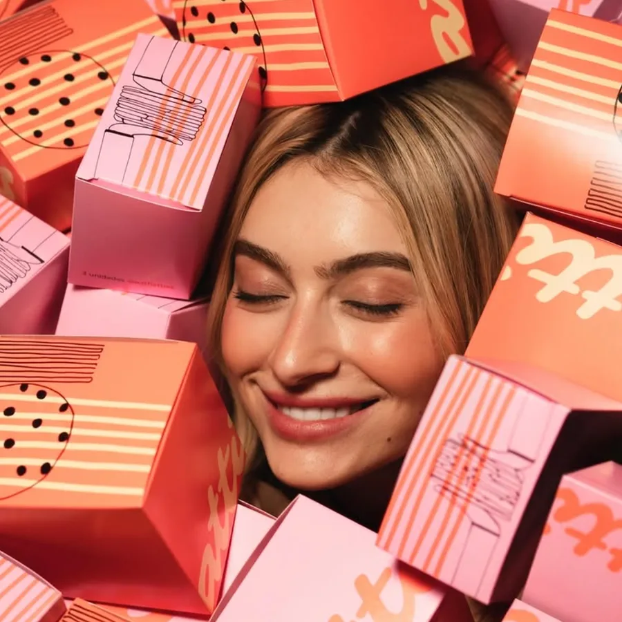 Mulher sorrindo no meio de caixas rosa e laranja da Flatties.