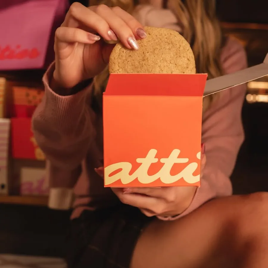 Mão tirando um cookie de uma caixa laranja da Flatties.